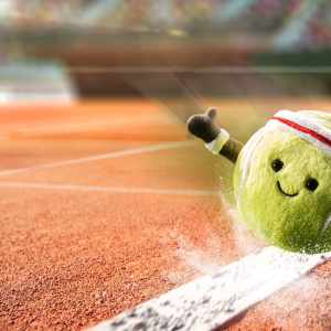 Jellycat amuseable tennis ball, yellow with white lines and seats bands on tennis court